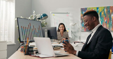 Office workers sit at their desks in front of computer monitors, not attending to their duties, using phones, browsing social media, chatting with friends, a break from work, talking, laughing