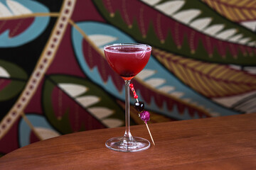 Elegant Red Cocktail with Berry and Flower Garnish in a Coupe Glass on Wooden Table