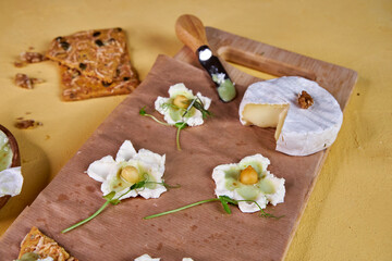 creative serving cheese board with soft cheese, honey and floral decoration on a yellow background
