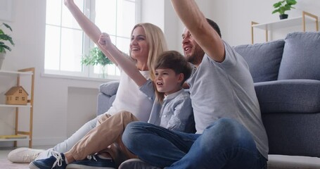 Happy family with a kid watching a soccer match on TV and celebrates a goal together. Moment of leisure at home highlights the excitement and joy of enjoying sports as a family unit.
