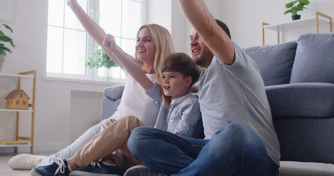 Happy family with a kid watching a soccer match on TV and celebrates a goal together. Moment of leisure at home highlights the excitement and joy of enjoying sports as a family unit.