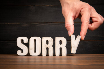 Hand Placing SORRY Text on Wooden Desk