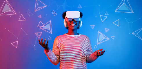 African girl with VR glasses standing at blue and pink background and looking at floating geometric shape. Excited person searching and entering visual reality world. Technology innovation. Ingenuity.