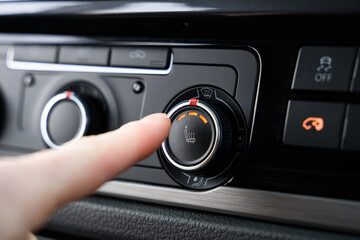 Finger about to press the heated seats button inside a car