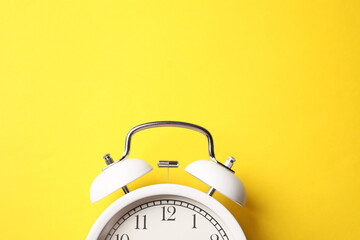 White alarm clock on yellow background, top view. Space for text