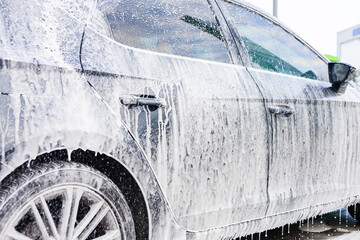 Car washing process with soap foam at a local service station during the day