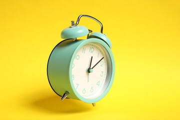 Turquoise alarm clock in air on yellow background