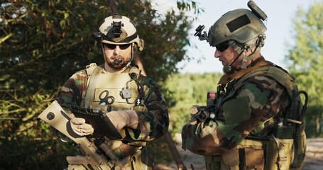 Soldiers in full combat gear, with helmets and rifles slung over their shoulders, analyze action...