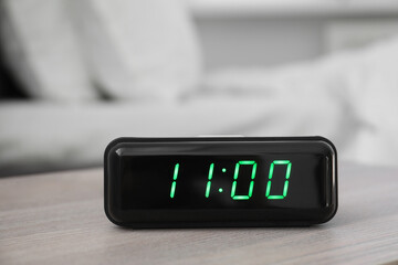 Digital alarm clock showing 11:00 o'clock on bedside table indoors