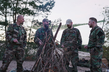 Fototapeta premium Military personnel dressed in camouflage stand around a campfire, frying sausages, laughing, and telling stories as they relax after duty and hunting on the base.