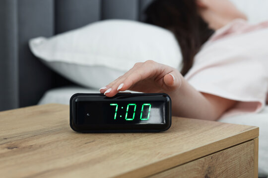 Woman turning off digital alarm clock on bedside table indoors, closeup