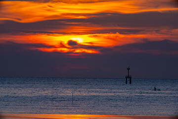 Fototapeta premium A striking seascape capturing the vivid hues of a sunset sky blending orange, red, and purple over the calm ocean. A navigation tower stands against the horizon, adding depth and dramatic scene. .