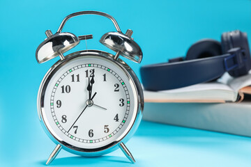 Alarm clock, books and headphones on light blue background