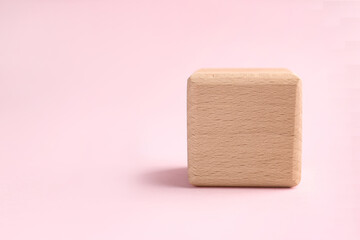 One wooden cube on pink background, closeup. Space for text
