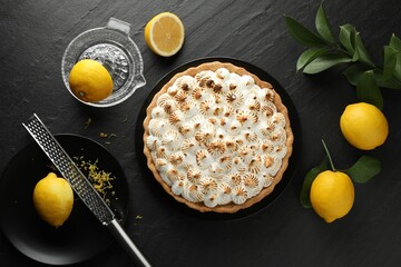 Delicious meringue pie, lemons, grater and squeezer on black textured table, flat lay