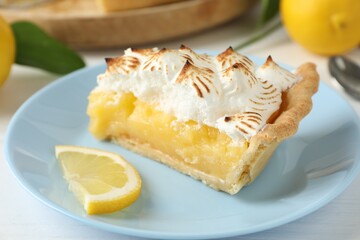 Piece of delicious pie with browned meringue and slice of lemon on white table, closeup