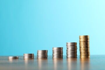 Stacks of different coins on table against light blue background, closeup. Space for text