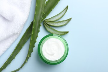 Moisturizing cream with extract of aloe vera, towel and leaves on light blue background, flat lay. Space for text