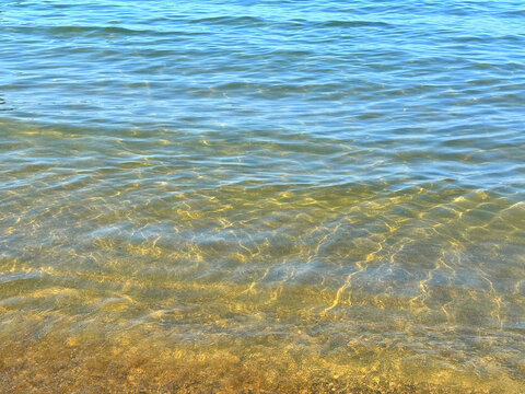 Gentle sea waves with sun reflections on sand beach.