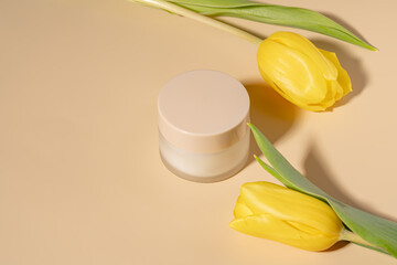 Elegant skincare cream with yellow tulips on beige background
