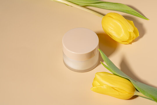 Elegant skincare cream with yellow tulips on beige background