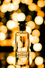 Elegant glass perfume bottle with black cap, set against a blurred golden bokeh background,...