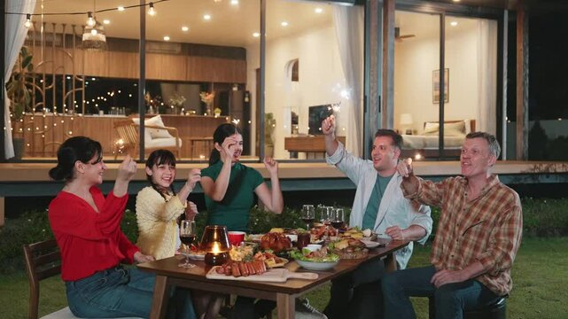 Happy family holding glowing sparkler in holiday celebration party at night. Lovely member enjoy playing spark together. Outdoor activity to cross generation gap strengthen family bond. Divergence.