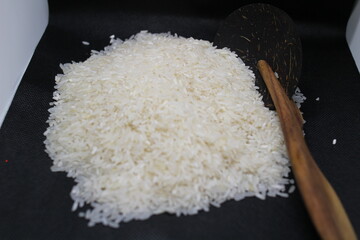 A close-up of uncooked white rice with a traditional wooden rice paddle on a dark textured background. The detailed shot highlights the texture and purity of the rice, ideal for food-related concepts.