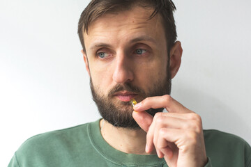 Man holding capsule near his lips, wearing green sweater, illustrating concept of taking vitamins, supplements, or medication for health wellness, isolated white background
