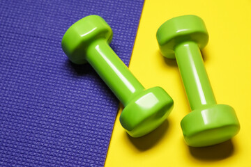 Dumbbells and fitness mat on yellow background, above view