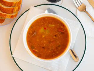 Spicy stewed lentils with suasage and vegetables with thick tomato sauce served in white plate. Typical Spanish cuisine