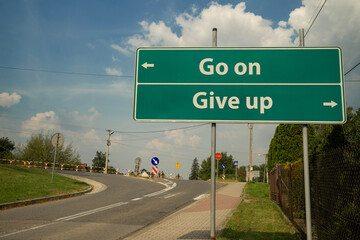 Drogowskaz przy drodze ze strzałkami w lewo oraz w prawo, z napisami: GO ON, GIVE UP. © siwyk