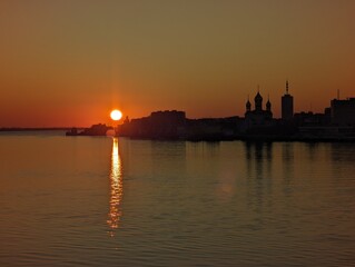 Fototapeta premium A stunning sunset lights up the calm waters, showcasing silhouettes of buildings against vibrant sky colors