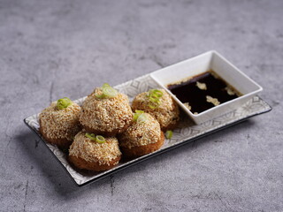 Crispy fried dumplings topped with spring onions, served with soy dipping sauce on a rectangular plate, styled in an elegant Asian dining setup.