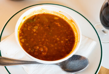 Portion of tratitional Spanish lentil soup with chorizo, sopa de lentejas, served on table.
