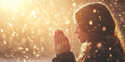 A woman is praying with hands clasped under falling sunlight snow