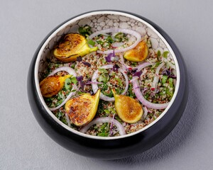 Quinoa salad with grilled figs, onion rings, and fresh herbs served in a black bowl, representing healthy and gourmet cuisine