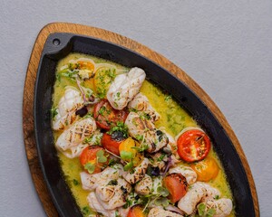 Grilled calamari with cherry tomatoes and herbs, served on a hot plate with sauce for an elegant Mediterranean seafood presentation