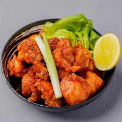 Crispy fried chicken served in a bowl with lettuce, lemon wedge, and celery stick, coated in a golden spicy glaze for a tasty presentation