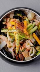 Asian seafood stir-fry with shrimp, vegetables, and noodles served in a black bowl, garnished with spices for a gourmet presentation