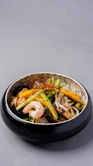 Asian seafood stir-fry with shrimp, vegetables, and noodles served in a black bowl, garnished with spices for a gourmet presentation
