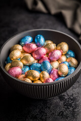 Chocolate easter eggs wrapped in multi colored foil in bowl on black table.