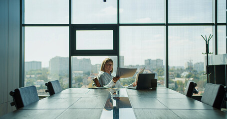 A businesswoman analyzing financial graphs in a modern office with panoramic city views,...
