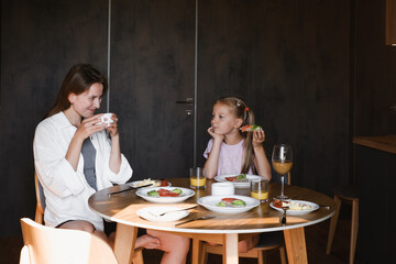 Mother and daughter having meal together in a stylish, contemporary hotel or home. Family eating delicious breakfast on the kitchen