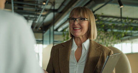 Obraz premium A professional businesswoman smiling confidently while holding a clipboard during a conversation in a modern office setting, showcasing positivity and professionalism