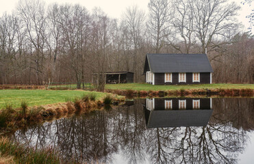Swedish forest cabin by a reflective pond in the countryside. Black traditional swedish house 