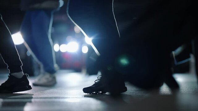 Low angle side view unrecognizable people crowd feet shoes steps busy street. Many pedestrians walking crowded crosswalk backlit with car headlights. Evening rush hour legs asphalt zebra crossing