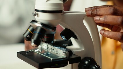 African american scholar studies medical science in a college library, doing research on viruses using a microscope. Girl works on exam preparation for success in a scientific career. Camera B.