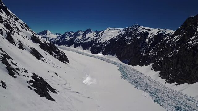 Sunlight illuminating Pers glacier surface, revealing pristine white landscape with dramatic mountain terrain and glacial features under bright blue sky
