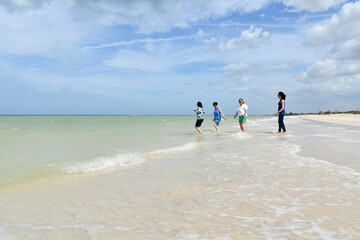 Four Latin American women of different ages walk on the beach at the seashore on a sunny day.